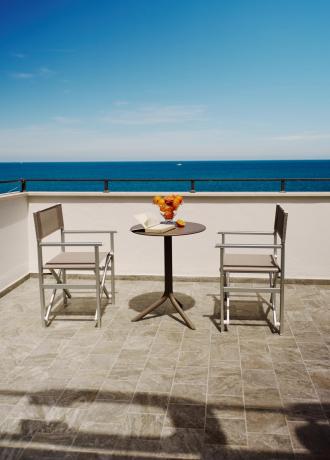 Terrace with sea view, two chairs, table with book and fruit.
