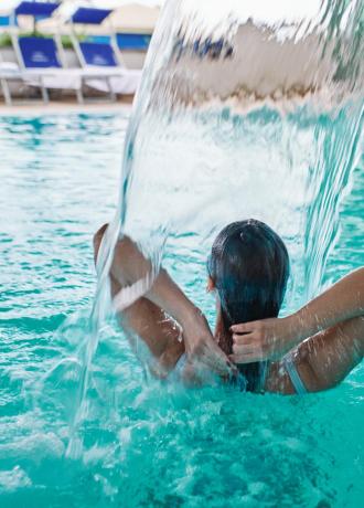 Person in a pool under a waterfall.
