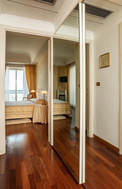 Hotelzimmer mit Bad, Holzboden, großer Spiegel.