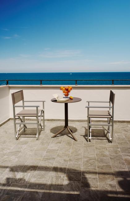 Terrazza con vista mare, due sedie, tavolo con libro e frutta.