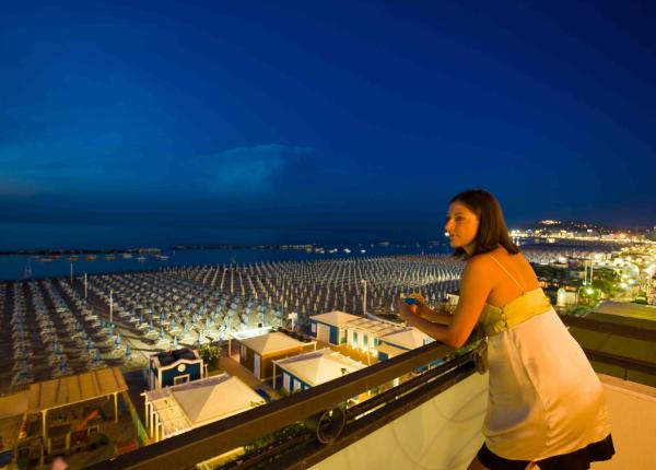 Frau auf Terrasse mit Blick auf Meer und nächtlichen Strand.