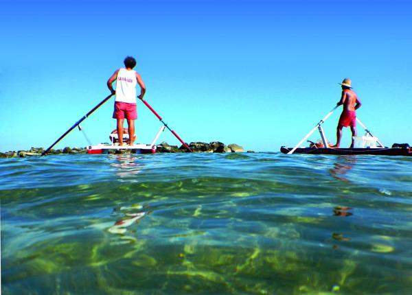 Zwei Personen auf Tretbooten im Meer.