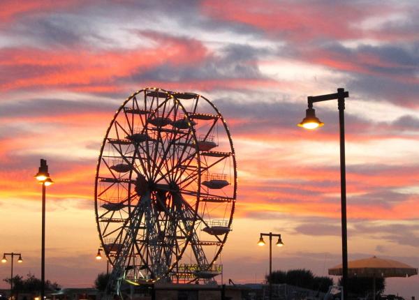 Ruota panoramica al tramonto con cielo colorato e lampioni accesi.