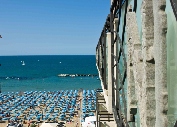 Plage bondée avec parasols bleus et mer calme.