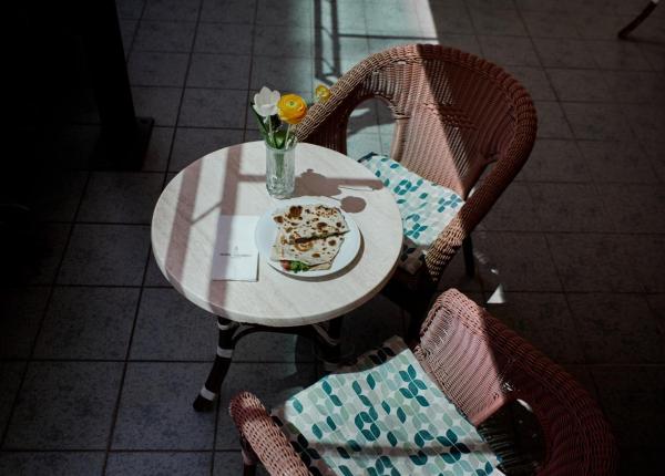 Tisch mit Blumen, Teller und Korbstühlen auf einer Terrasse.