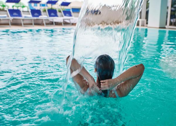 Person in a pool under a waterfall.