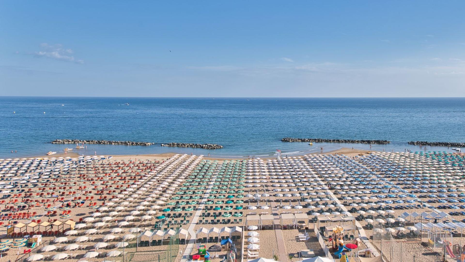 Spiaggia affollata con ombrelloni colorati e mare calmo.