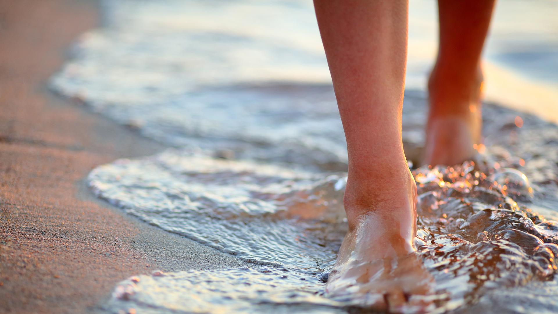 Pieds marchant dans l'eau sur la plage au coucher du soleil.