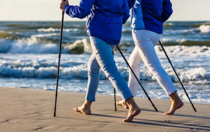 Two people walking on the beach with trekking poles.