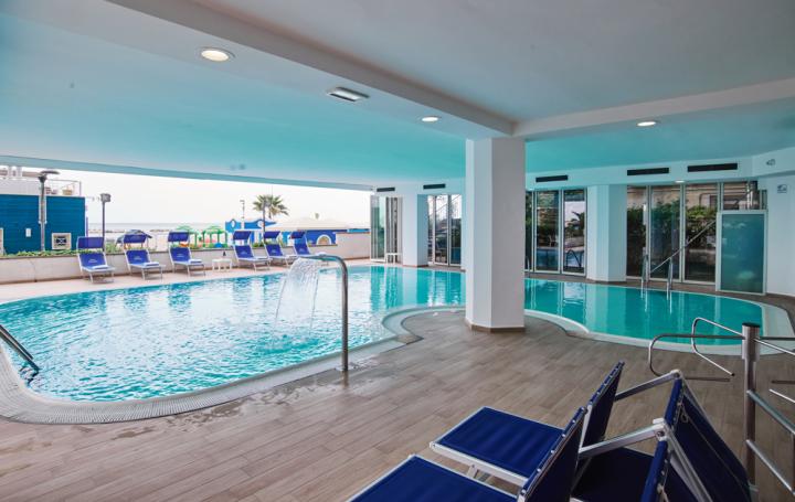 Piscina coperta con lettini e vista mare.