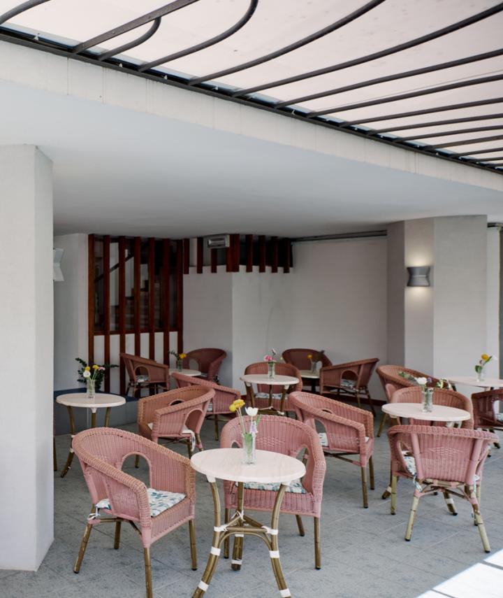 Terrasse couverte avec tables et chaises en osier, décorée de fleurs.