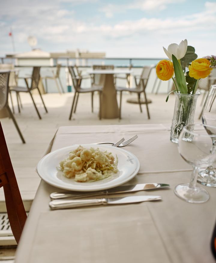 Piatto di pasta su tavolo con vista mare e fiori.