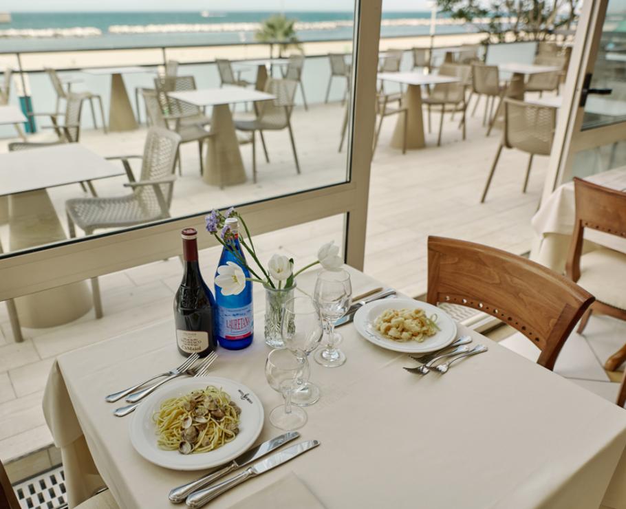 Table set with sea view, wine, and pasta dishes.