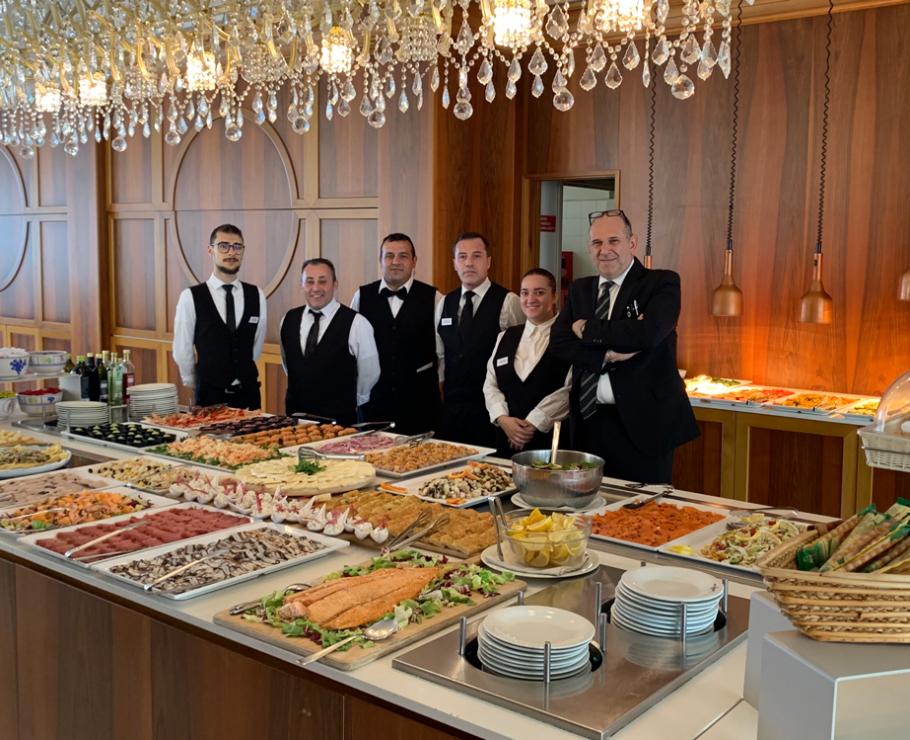Elegant buffet with uniformed staff, assorted dishes, and sparkling chandeliers.