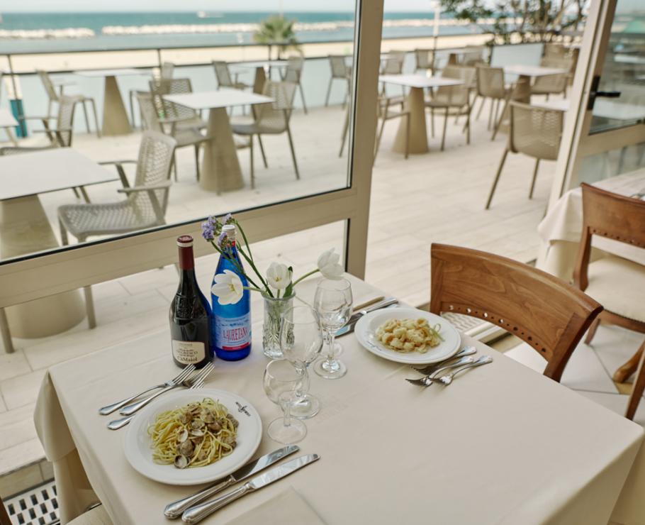 Table dressée avec vue sur mer, vin et plats de pâtes.